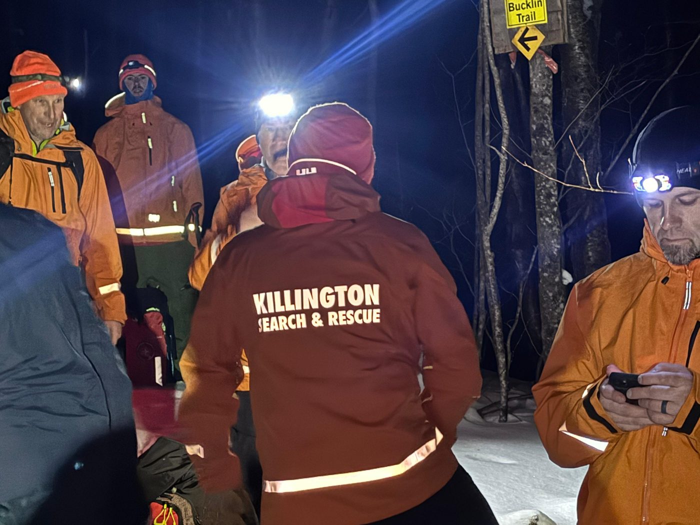KSAR members in headlamps and orange jackets gather on a snowy trail at night, near the sign for Bucklin Trail