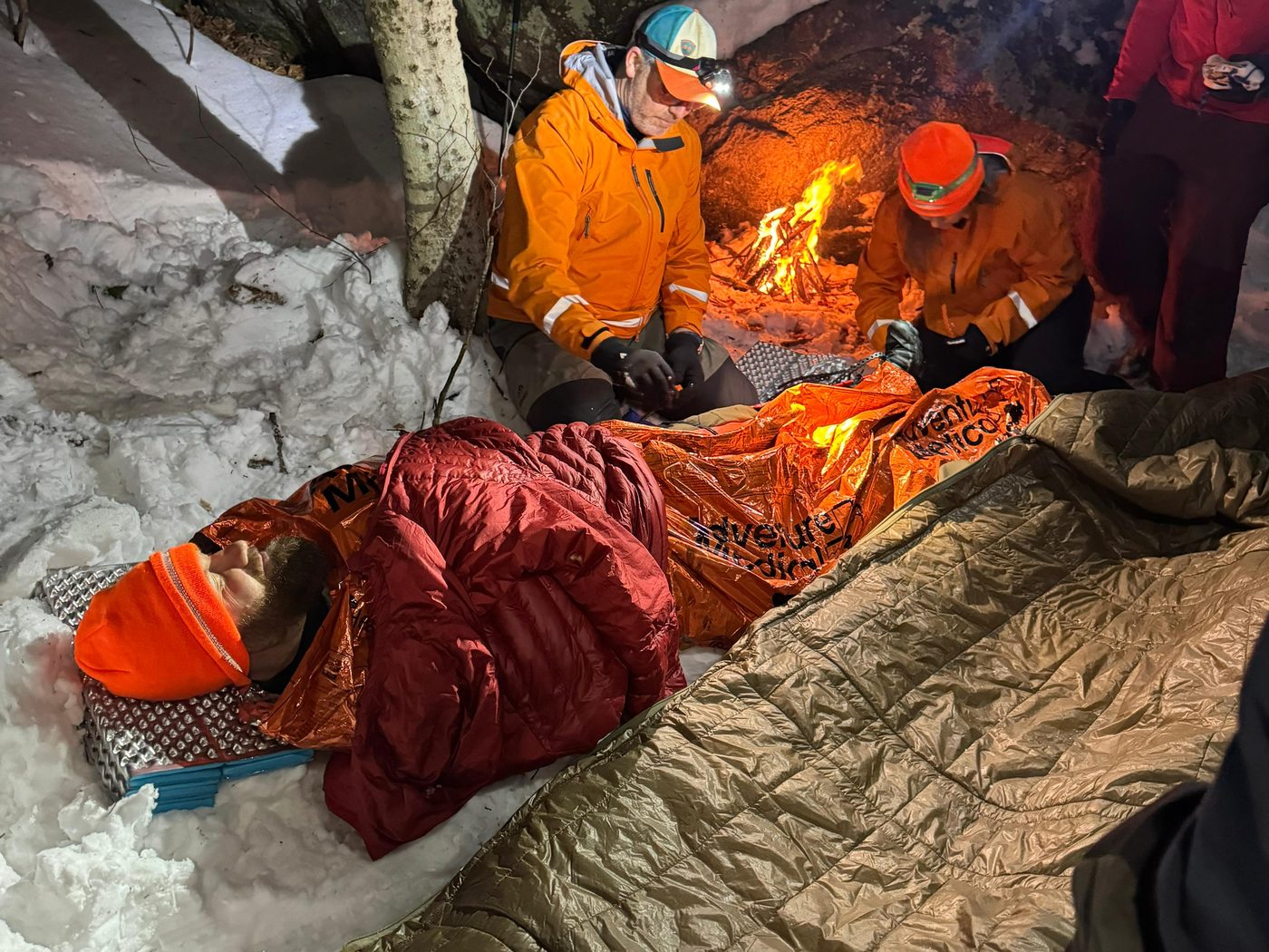 KSAR members tend a volunteer patient wrapped in a bivy sack and sleeping bag beside a small fire during a night training
