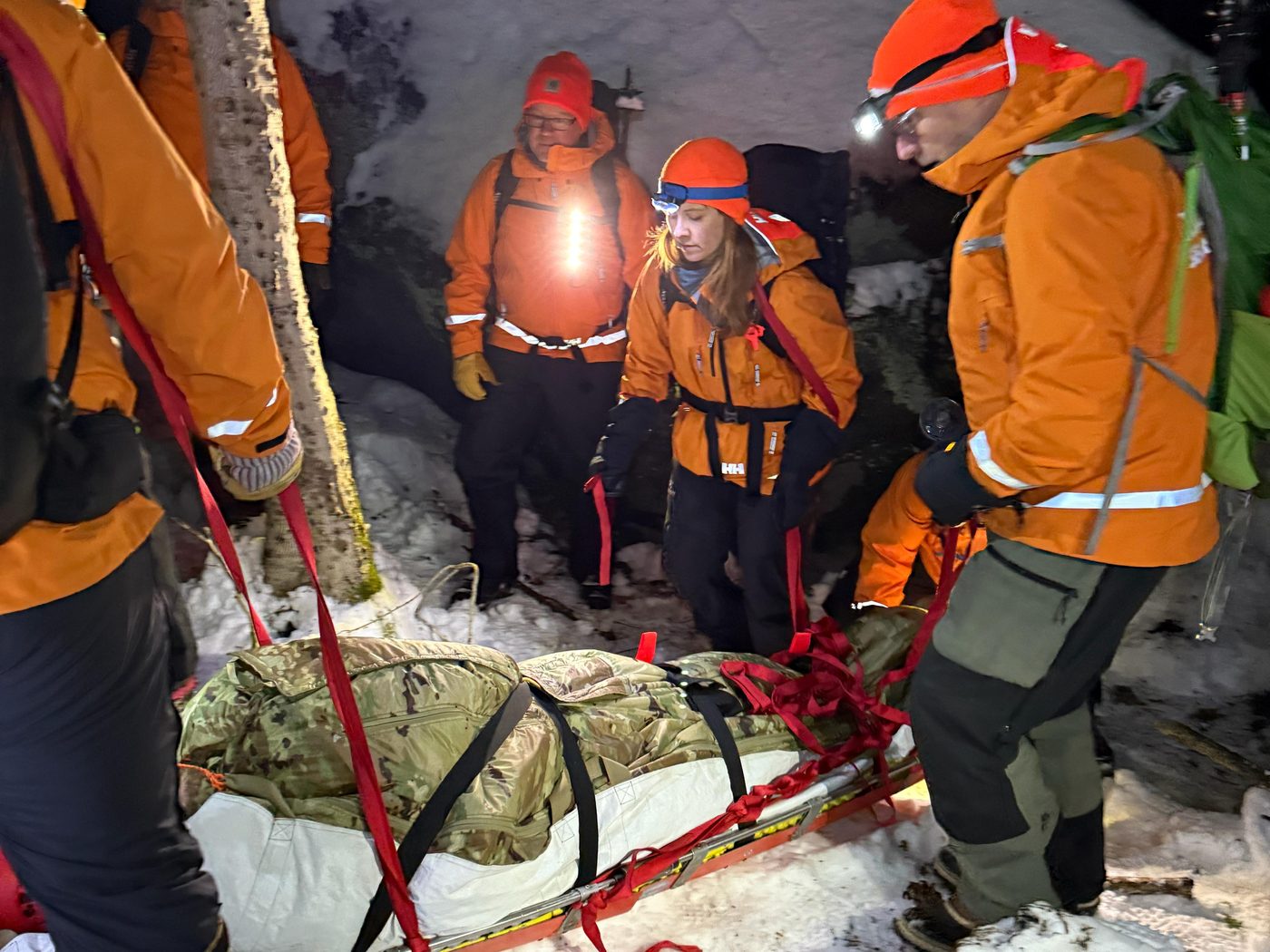 KSAR members in orange jackets and headlamps carry a litter with a volunteer patient through the snowy woods at night