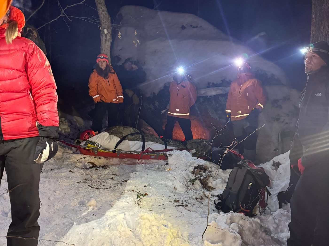 KSAR members with headlamps gather around a rescue litter on a snowy trail at night