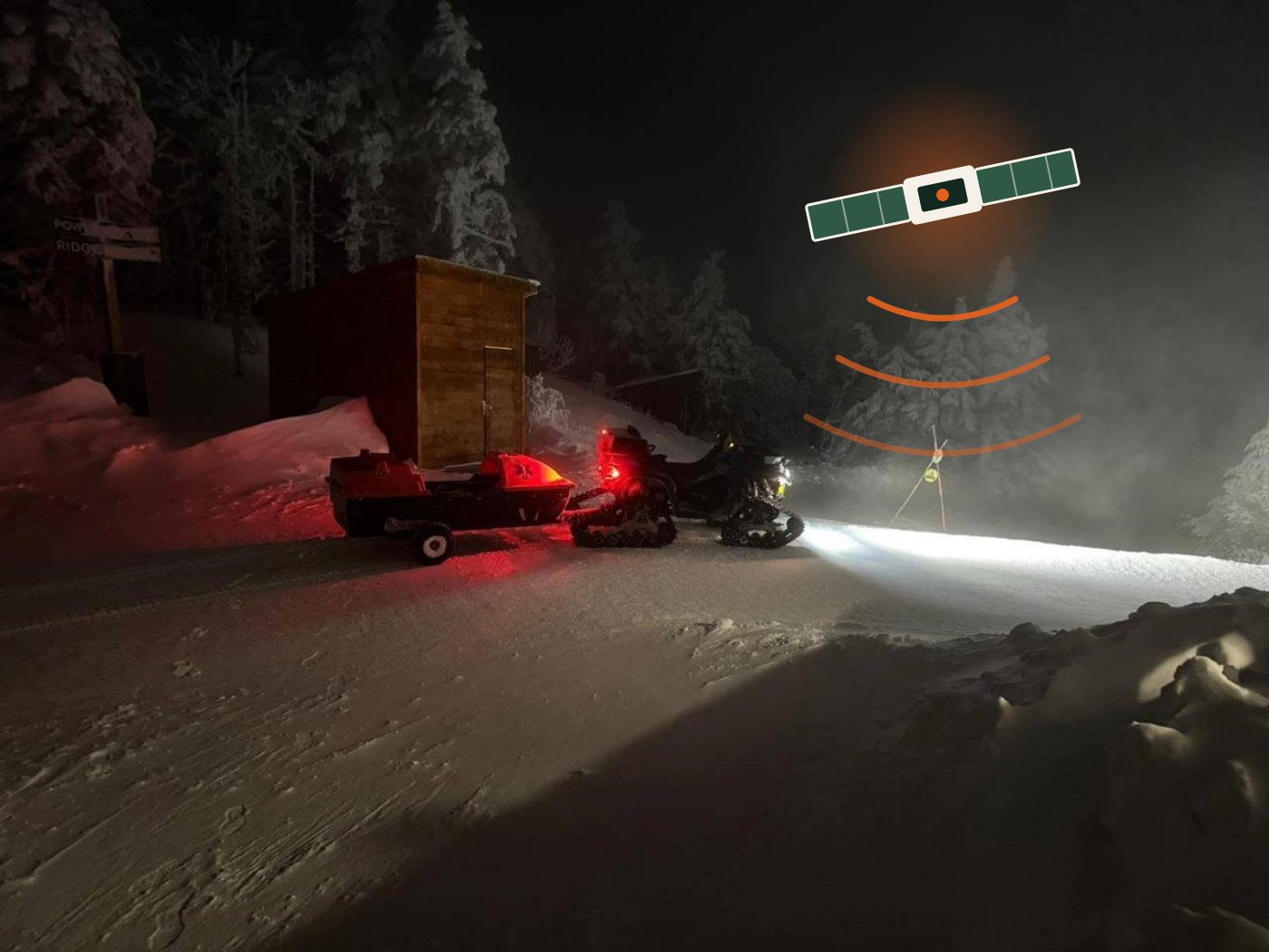 A KSAR snowmobile and rescue sled trailer parked on a snowy road at night with a satellite and signal graphic above