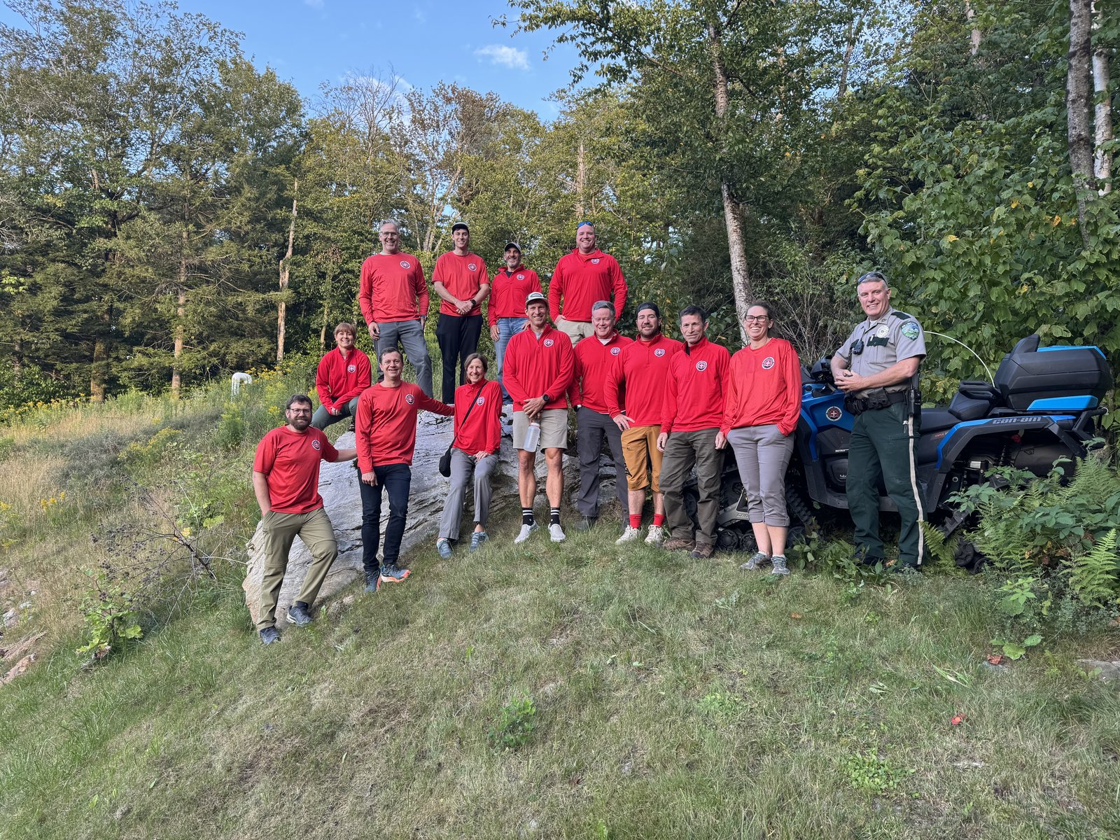 The KSAR team in red shirts posed on a boulder next to an ATV, with the Killington police chief