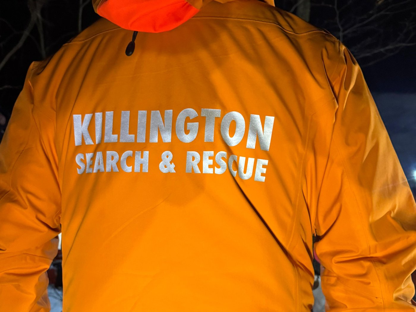 The back of an orange KSAR jacket reading Killington Search and Rescue during a winter night training